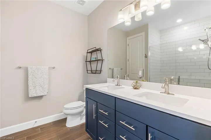 Full bath with double vanity, tiled shower, and wood finished floors
