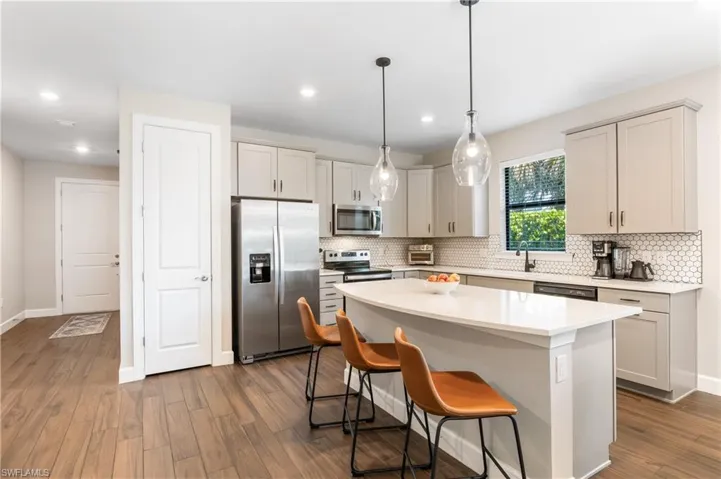 Kitchen featuring stainless steel appliances, a center island, a breakfast bar area, light countertops, and dark wood-style flooring