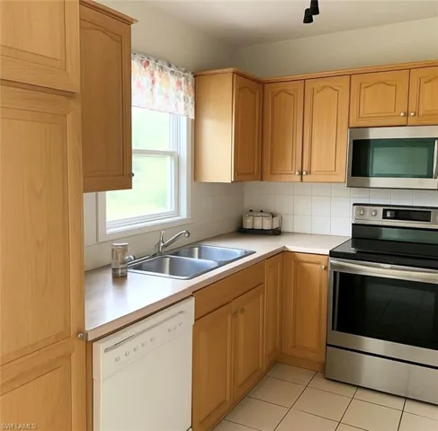 Kitchen with stainless steel appliances, light countertops, tasteful backsplash, light brown cabinets, and light tile patterned floors