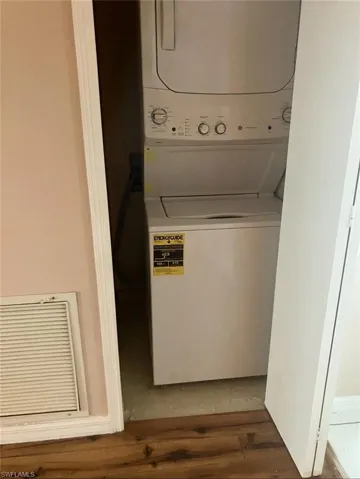 Laundry area with stacked washing machine and dryer and wood finished floors