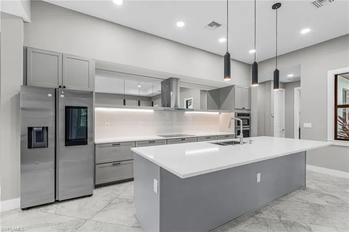Kitchen featuring gray cabinets, stainless steel appliances, an island with sink, hanging light fixtures, and tasteful backsplash