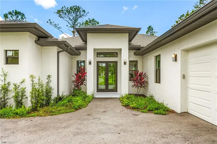 View of exterior entry with roof with shingles, an attached garage, and stucco siding