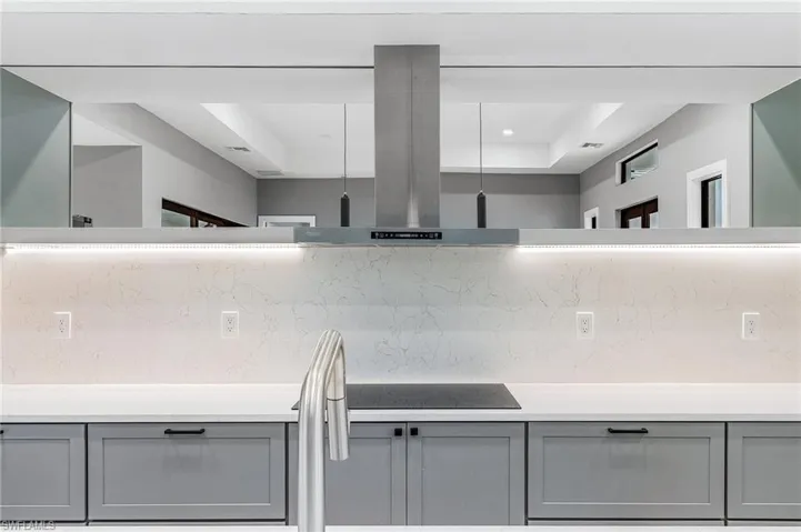 Kitchen featuring gray cabinetry, decorative backsplash, island exhaust hood, and light stone counters