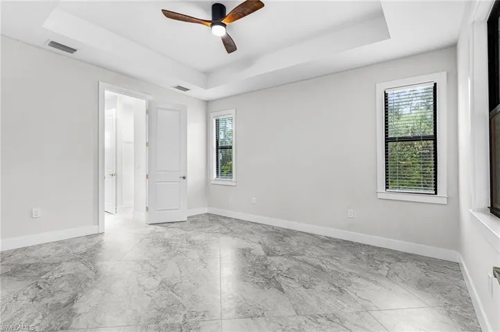 Unfurnished room with a tray ceiling, a ceiling fan, and light marble finish floors