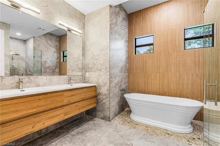 Full bathroom featuring tile walls, a marble finish shower, double vanity, and a soaking tub