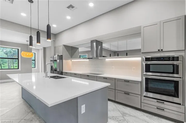 Kitchen with gray cabinetry, backsplash, decorative light fixtures, a large island with sink, and recessed lighting