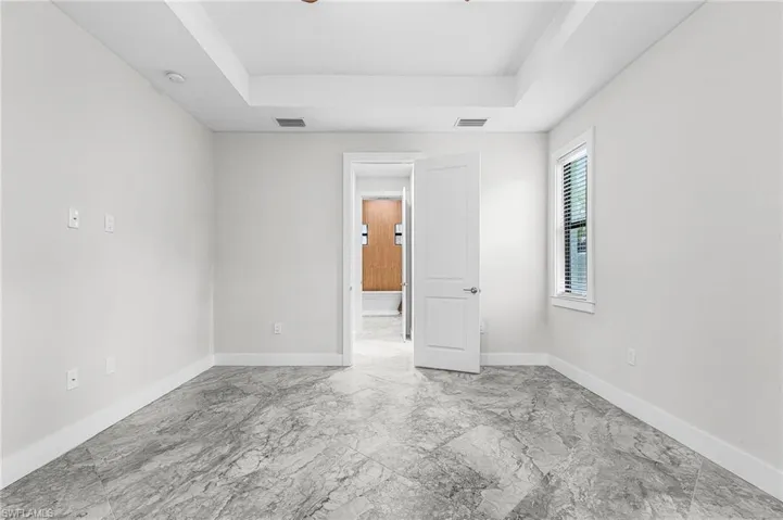 Unfurnished bedroom with a tray ceiling and light marble finish flooring
