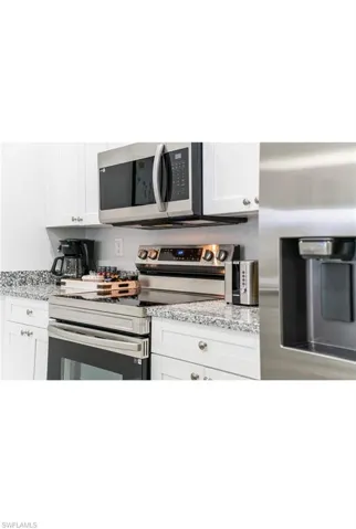 Kitchen with light stone counters, appliances with stainless steel finishes, and white cabinetry