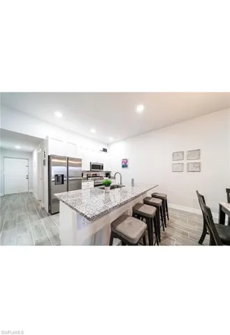 Kitchen with a breakfast bar area, light stone countertops, light hardwood / wood-style flooring, appliances with stainless steel finishes, and white cabinetry