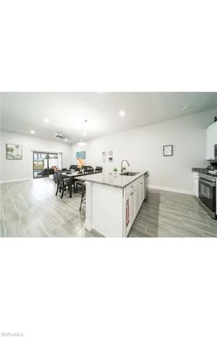 Kitchen featuring white cabinets, appliances with stainless steel finishes, light stone counters, sink, and a center island with sink
