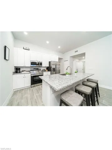 Kitchen with light stone countertops, a kitchen island with sink, a kitchen bar, stainless steel appliances, and white cabinets