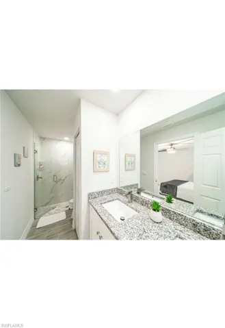 Bathroom featuring vanity, hardwood / wood-style flooring, walk in shower, and ceiling fan