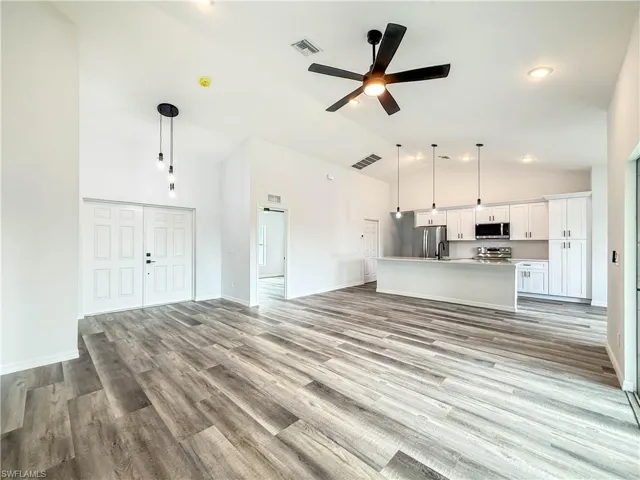 Unfurnished living room with high vaulted ceiling, a ceiling fan, and light wood-type flooring