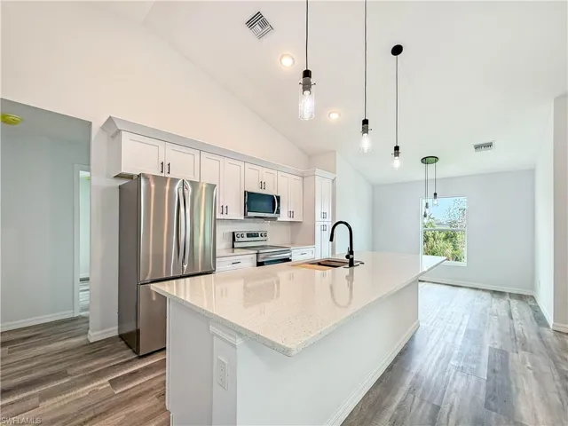 Kitchen with stainless steel appliances, hanging light fixtures, white cabinets, light stone counters, and high vaulted ceiling