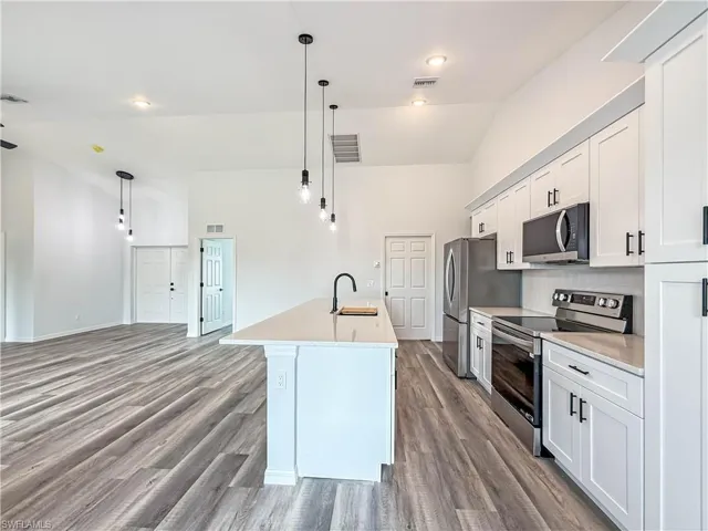 Kitchen featuring appliances with stainless steel finishes, white cabinetry, high vaulted ceiling, hanging light fixtures, and a kitchen island with sink