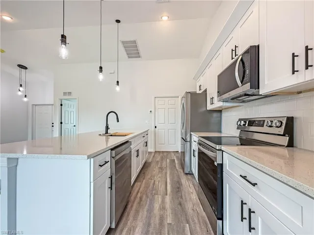 Kitchen featuring stainless steel appliances, light stone countertops, and white cabinetry