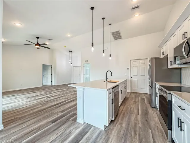 Kitchen with white cabinetry, open floor plan, appliances with stainless steel finishes, high vaulted ceiling, and pendant lighting