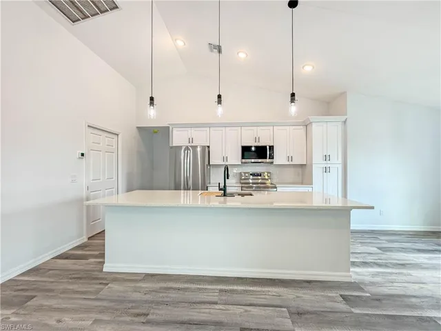 Kitchen with stainless steel appliances, white cabinets, hanging light fixtures, light wood-type flooring, and high vaulted ceiling