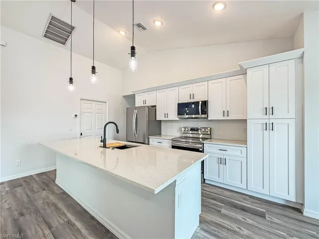 Kitchen featuring pendant lighting, stainless steel appliances, dark wood-style floors, light stone counters, and white cabinetry