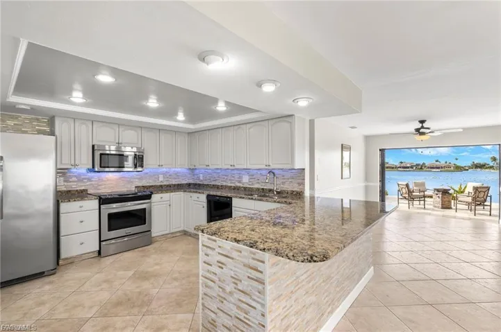 Kitchen with tasteful backsplash, dark stone countertops, appliances with stainless steel finishes, light tile patterned floors, and recessed lighting