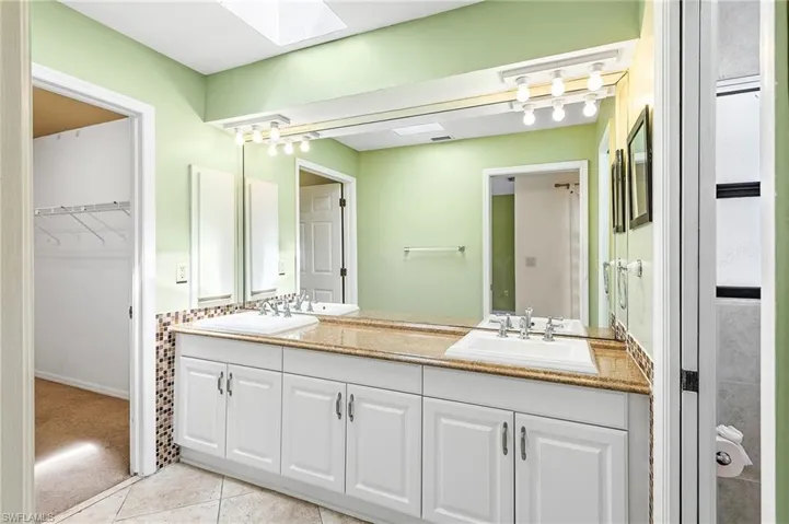Primary Full bathroom featuring a skylight, double vanity, light tile patterned floors, a walk in closet, and light colored carpet
