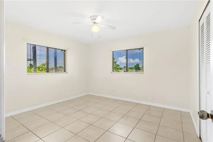 Unfurnished Guest bedroom with a closet, multiple windows, a ceiling fan, and light tile patterned floors