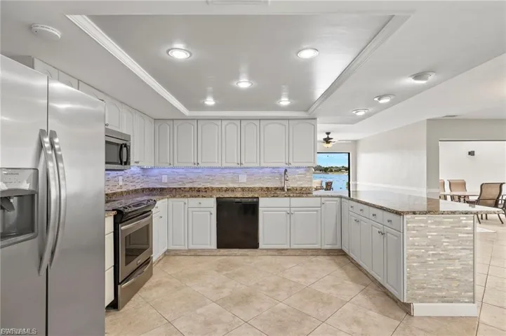 Kitchen featuring a tray ceiling, stainless steel appliances, decorative backsplash, dark stone counters, and recessed lighting