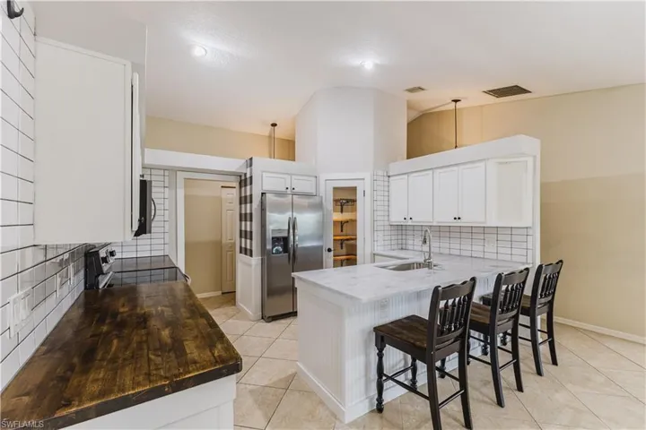 Kitchen featuring white cabinetry, stainless steel appliances, a breakfast bar area, backsplash, and a peninsula