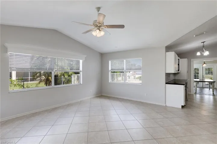 Unfurnished living room with lofted ceiling, a ceiling fan, light tile patterned floors, and a chandelier