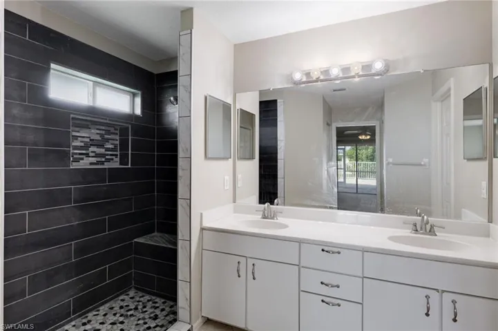 Full bath with healthy amount of natural light, double vanity, and a tile shower