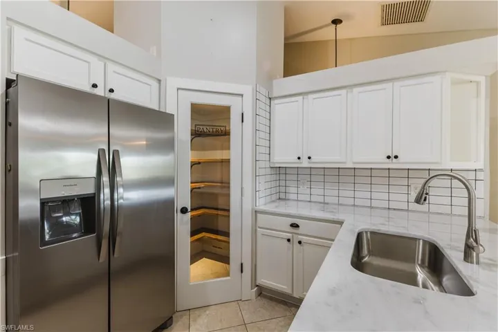 Kitchen with stainless steel fridge, white cabinetry, light stone countertops, decorative backsplash, and light tile patterned floors