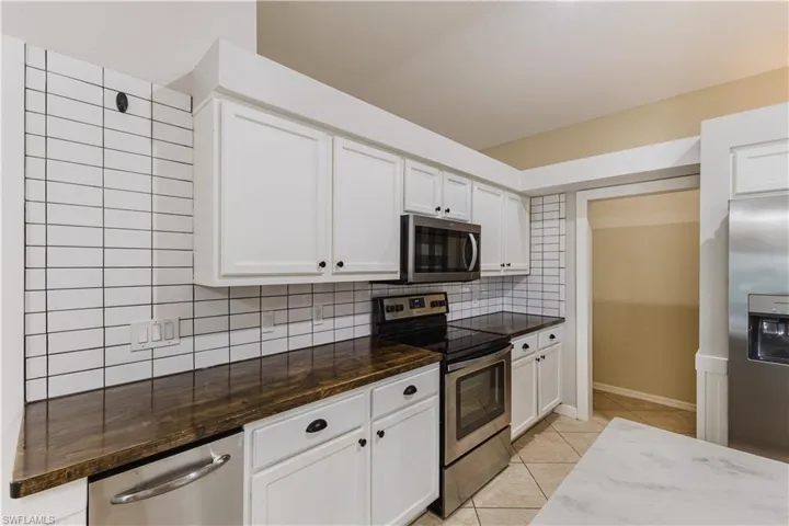 Kitchen with stainless steel appliances, backsplash, white cabinets, and light tile patterned floors