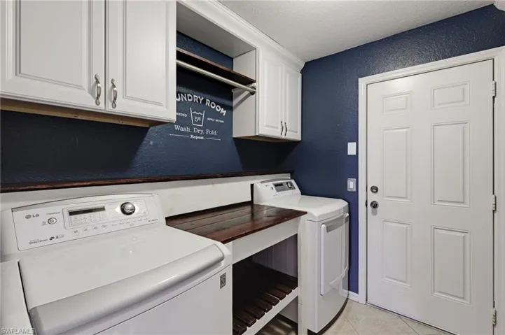 Laundry room featuring a textured wall, a textured ceiling, light tile patterned floors, cabinet space, and washer and clothes dryer