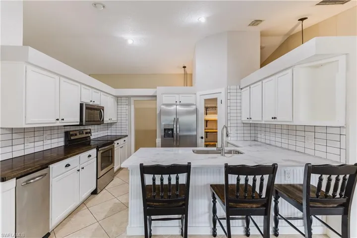 Kitchen with stainless steel appliances, white cabinets, tasteful backsplash, a kitchen bar, and a peninsula