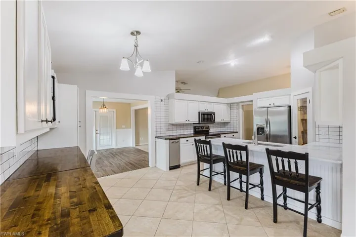 Kitchen with white cabinets, a kitchen breakfast bar, tasteful backsplash, lofted ceiling, and light tile patterned floors