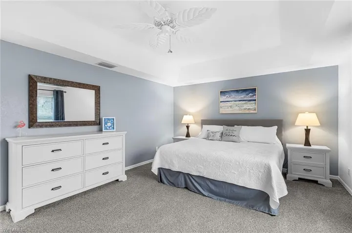 Bedroom with light colored carpet, ceiling fan, and a tray ceiling