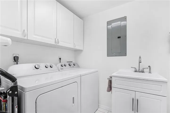 Laundry room featuring cabinet space, electric panel, washer and clothes dryer, and light tile patterned flooring