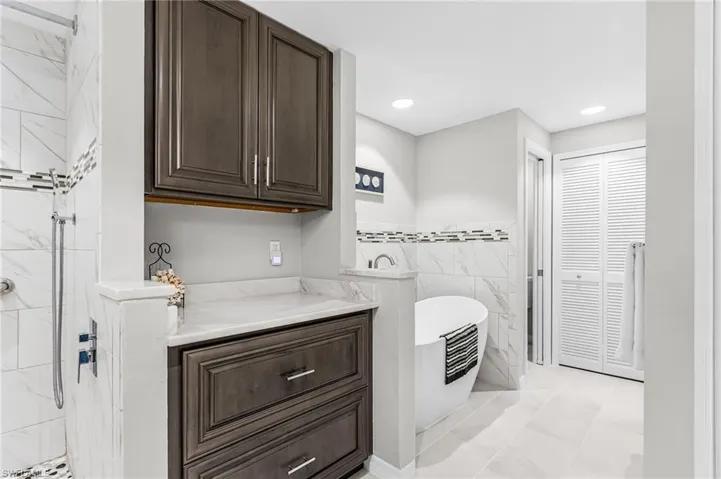 Full bath with a freestanding bath, a marble finish shower, a closet, light tile patterned floors, and recessed lighting
