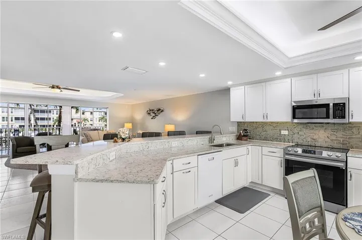 Kitchen with a ceiling fan, a tray ceiling, a kitchen bar, appliances with stainless steel finishes, and recessed lighting