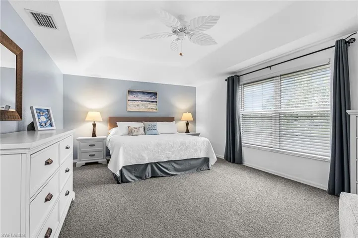 Bedroom featuring light carpet, a raised ceiling, and a ceiling fan