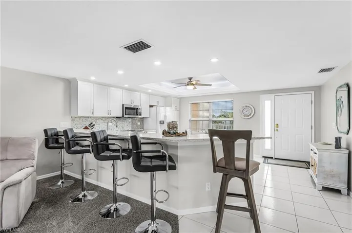 Kitchen featuring a raised ceiling, a peninsula, a breakfast bar area, decorative backsplash, and white cabinets