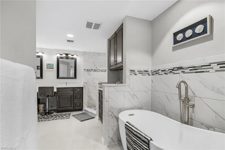 Full bath featuring tile walls, vanity, a freestanding tub, light tile patterned floors, and recessed lighting