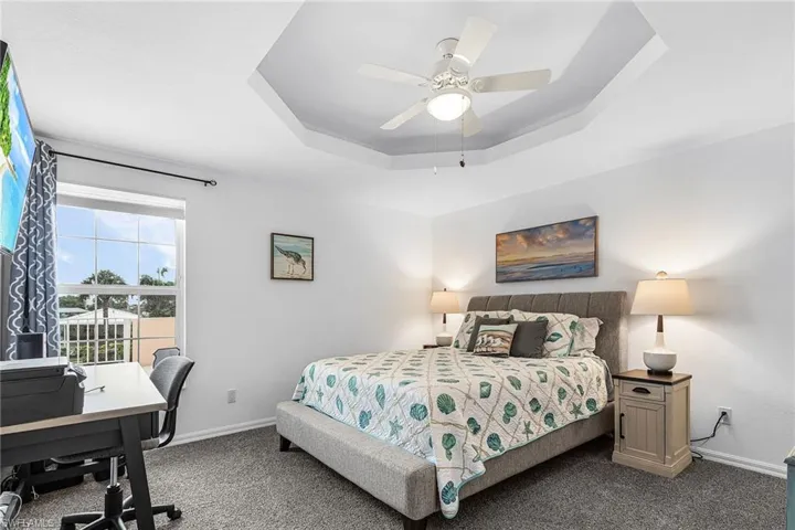 Carpeted bedroom with a tray ceiling, a desk, and ceiling fan