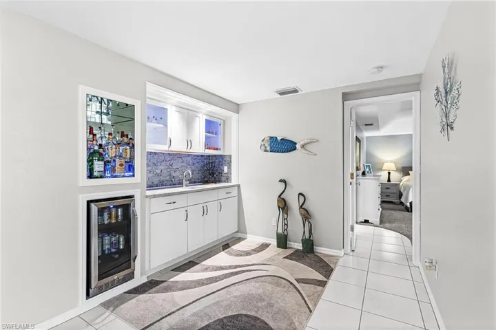 Indoor wet bar featuring white cabinets, beverage cooler, light tile patterned floors, and decorative backsplash