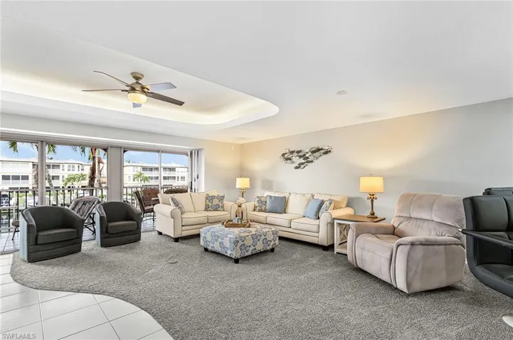 Living room featuring a raised ceiling, light tile patterned floors, a ceiling fan, and light carpet