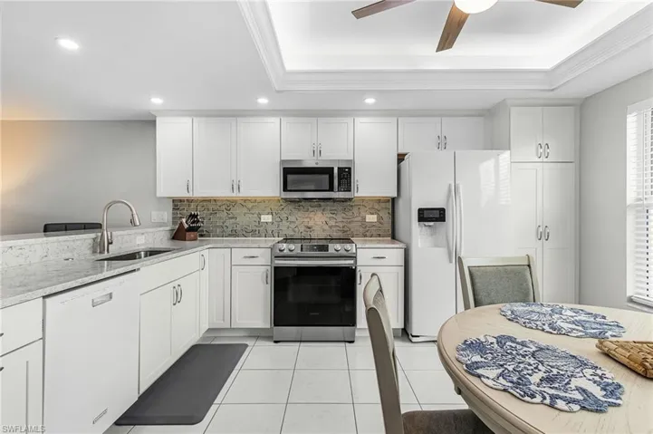 Kitchen featuring stainless steel appliances, a tray ceiling, tasteful backsplash, light tile patterned floors, and white cabinetry