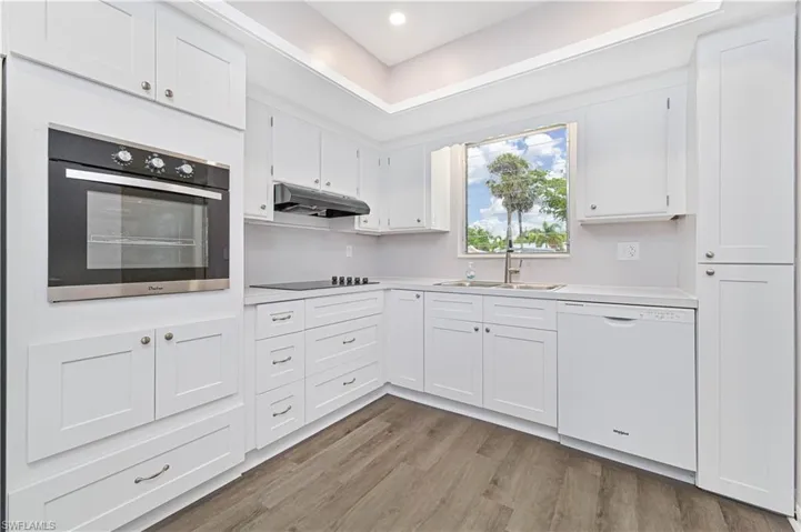 Kitchen with light countertops, white cabinetry, under cabinet range hood, black electric stovetop, and dishwasher