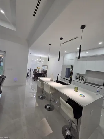 Kitchen with modern cabinets, white cabinetry, a breakfast bar, hanging light fixtures, and light stone counters