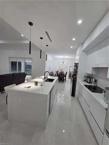 Kitchen with modern cabinets, light stone counters, a large island with sink, stovetop, and fridge