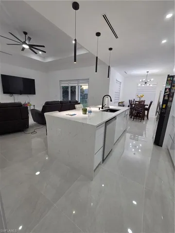 Kitchen featuring open floor plan, light stone countertops, a kitchen island with sink, refrigerator, and pendant lighting
